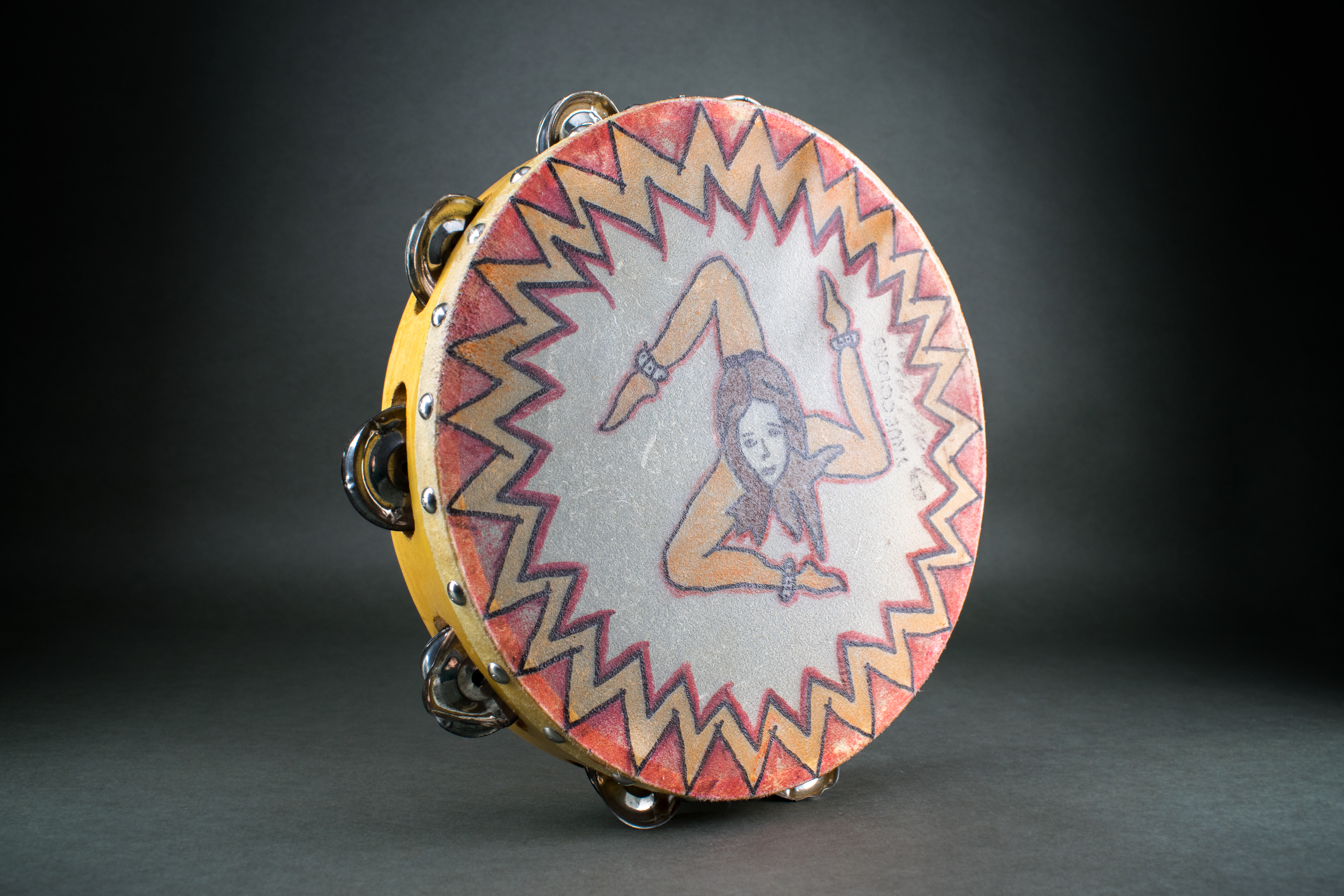 Tambourine for playing the Tarantella, hand-painted, around 1985. DOMiD Archive, Cologne, E 0893,0002. The association Associazione Genitori Italiani di Colonia (“Association of Italian Parents in Cologne”) also included a folklore dance group. It was founded in 1981 and was dedicated to the Tarantella, a folk dance from southern Italy. In 2005 the association had 230 members. The history of origin says that the rapid rhythm of the tarantella should encourage patients bitten by a tarantula to dance quickly until they are completely exhausted. This is said to drive animal poison out of the body. A typical rhythm instrument is the tambourine, here adorned with the triskele of the flag of Sicily.