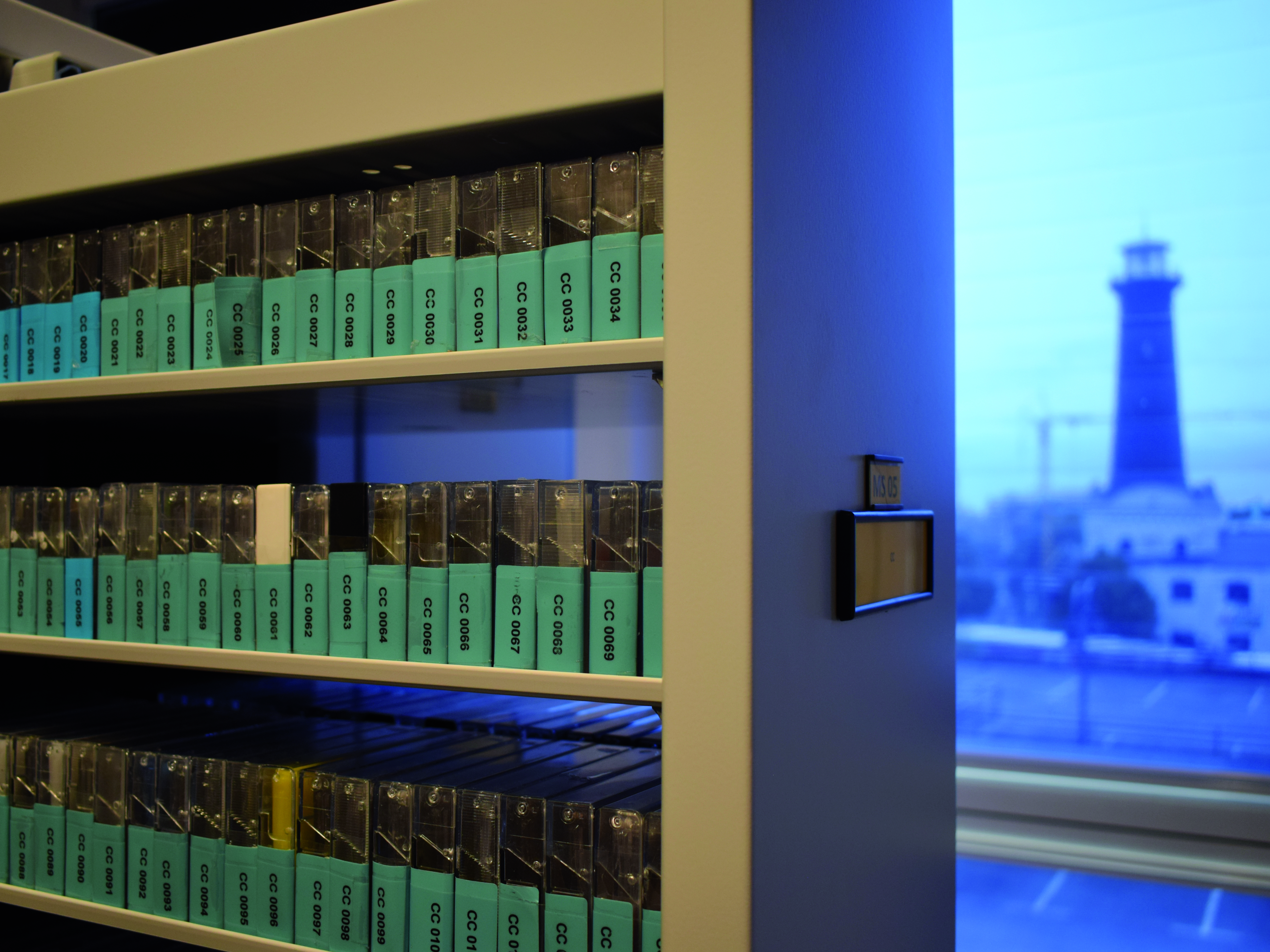 Kassetten in einem der DOMiD Depots; im Hintergrund der Leuchtturm in Köln-Ehrenfeld. Foto: DOMiD-Archiv, Köln